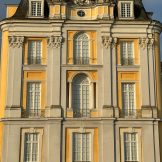 Draufsicht auf eine Flügelfront der Augustusburg. Angedeutete Seulen in grauem Stein auf gelben Hintergrund und weißen Fenstern