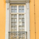 Außenansicht auf ein restauriertes Fenster mit grauer schön gestalterer Stein-Einfassung auf gelber Wand.